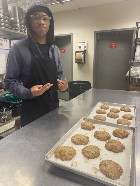 A baker standing beside trays of cookies in a kitchen.
